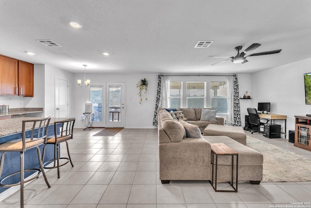 living area with light tile patterned floors, visible vents, ceiling fan with notable chandelier, and a textured ceiling