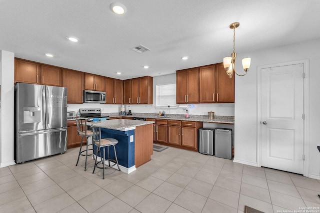 kitchen featuring visible vents, a kitchen island, appliances with stainless steel finishes, a kitchen breakfast bar, and brown cabinetry