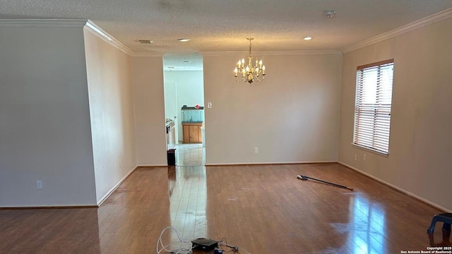 spare room featuring visible vents, a textured ceiling, hardwood / wood-style floors, crown molding, and baseboards