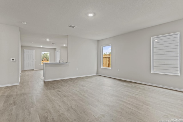 unfurnished living room featuring visible vents, baseboards, recessed lighting, light wood-style flooring, and a textured ceiling