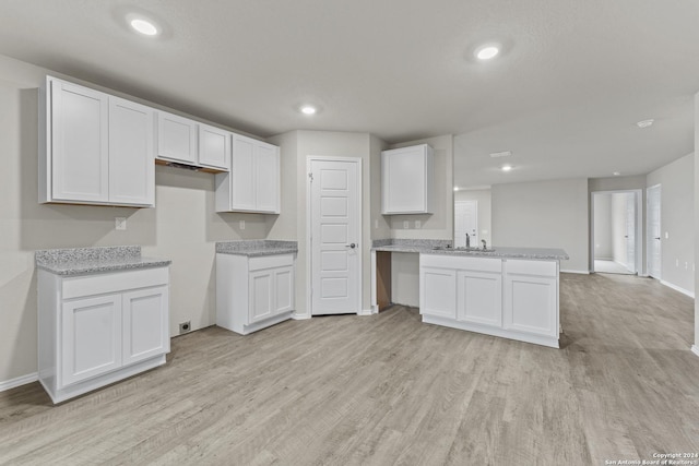 kitchen with a sink, recessed lighting, light wood-style floors, a peninsula, and white cabinets