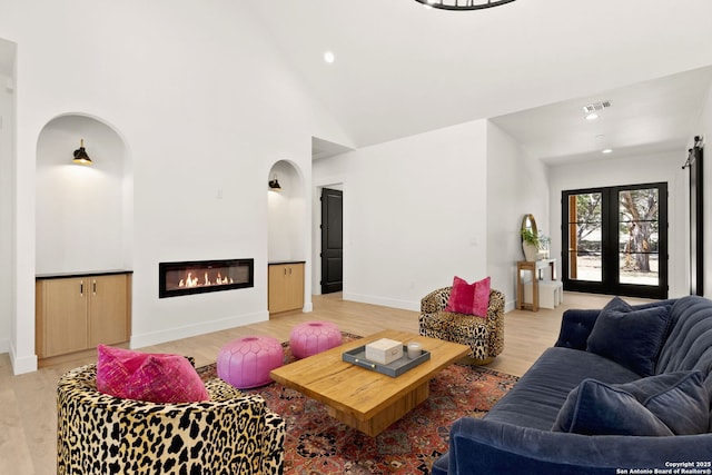 living room featuring baseboards, visible vents, high vaulted ceiling, light wood-style floors, and a glass covered fireplace