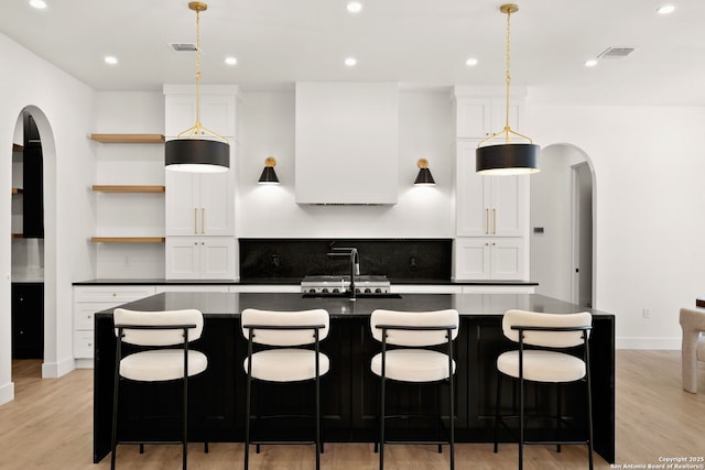 kitchen with dark countertops, visible vents, light wood-type flooring, arched walkways, and open shelves