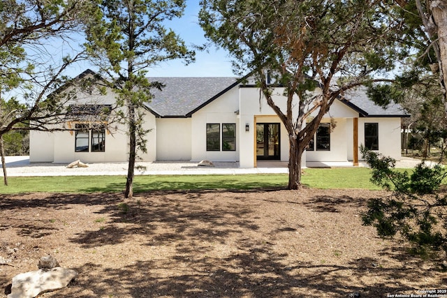 rear view of house featuring french doors, a lawn, and stucco siding