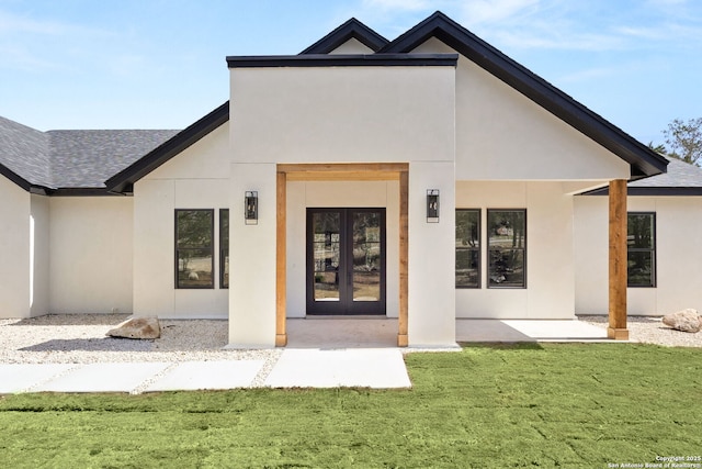 property entrance featuring stucco siding, french doors, a yard, and roof with shingles