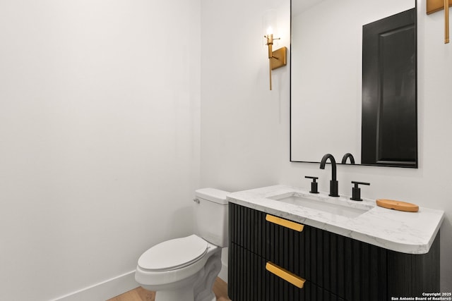 bathroom with vanity, toilet, wood finished floors, and baseboards