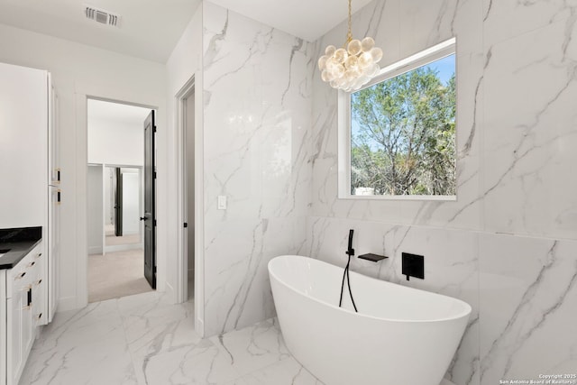 full bath featuring visible vents, marble finish floor, a freestanding bath, and stone wall