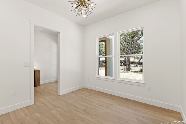 spare room featuring baseboards, a healthy amount of sunlight, light wood-style flooring, and an inviting chandelier