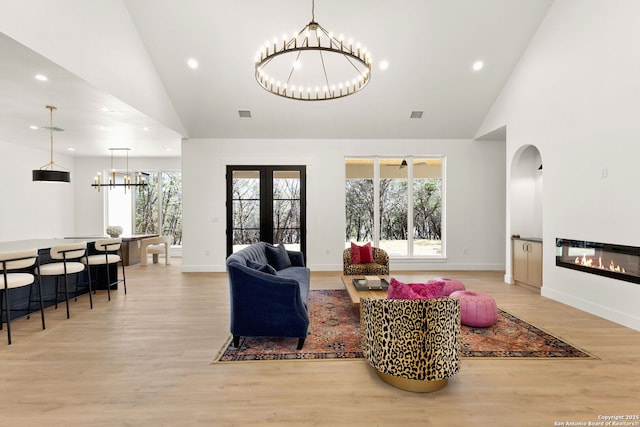 living room with a glass covered fireplace, light wood-style flooring, french doors, and a chandelier