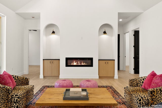 living room featuring baseboards, lofted ceiling, light wood-style floors, and a glass covered fireplace