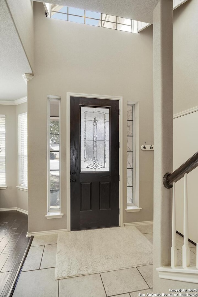 tiled foyer entrance featuring stairway, baseboards, a textured ceiling, and ornamental molding