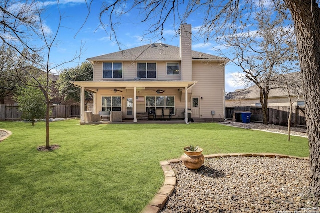 rear view of property with a lawn, a ceiling fan, a fenced backyard, a chimney, and a patio area