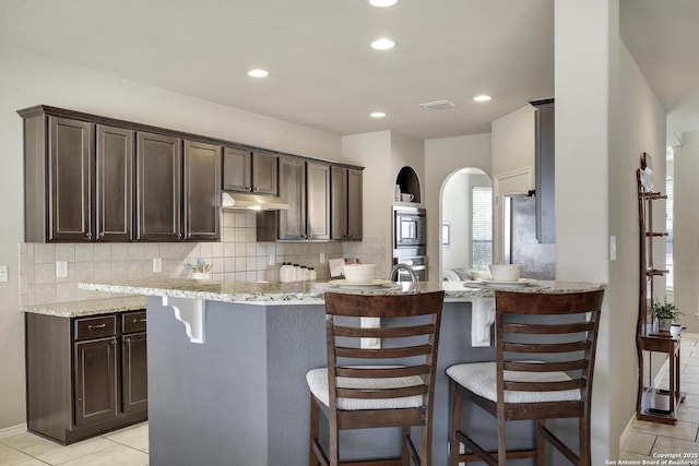 kitchen with visible vents, under cabinet range hood, backsplash, appliances with stainless steel finishes, and dark brown cabinets