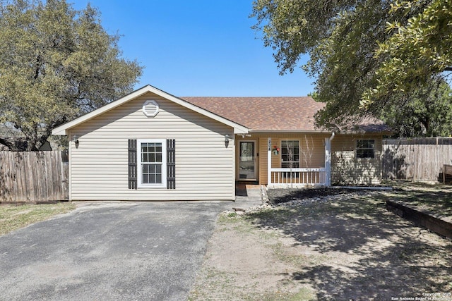 ranch-style house featuring a porch, a shingled roof, and fence