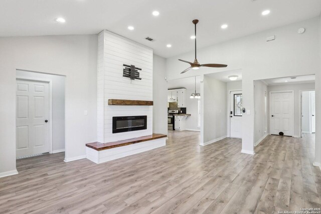 unfurnished living room with a ceiling fan, recessed lighting, light wood-style floors, a fireplace, and a towering ceiling