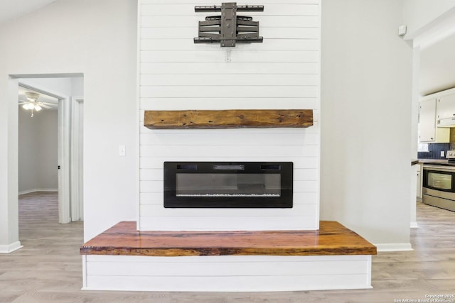 interior details featuring under cabinet range hood, wood finished floors, stainless steel electric range, a fireplace, and baseboards