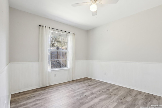 empty room featuring ceiling fan, wood finished floors, and wainscoting