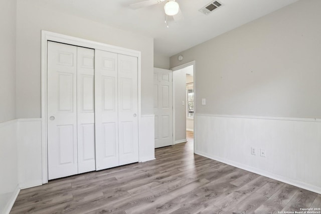 unfurnished bedroom with visible vents, a wainscoted wall, wood finished floors, a closet, and a ceiling fan