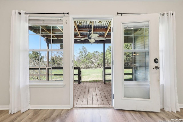 doorway featuring plenty of natural light, wood finished floors, baseboards, and ceiling fan