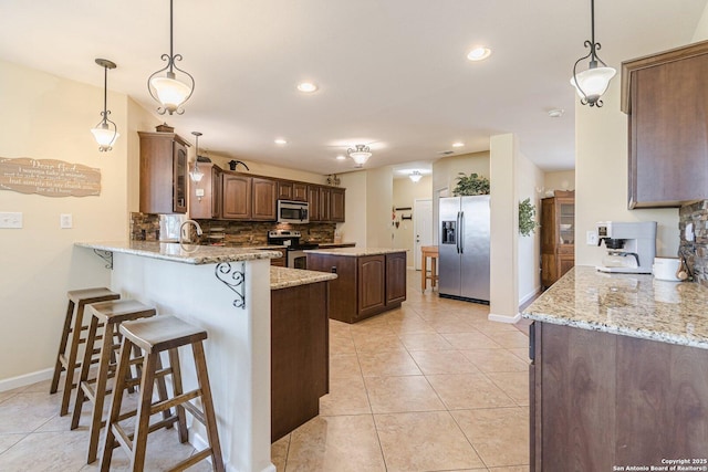 kitchen with light tile patterned floors, decorative backsplash, a peninsula, a kitchen breakfast bar, and stainless steel appliances