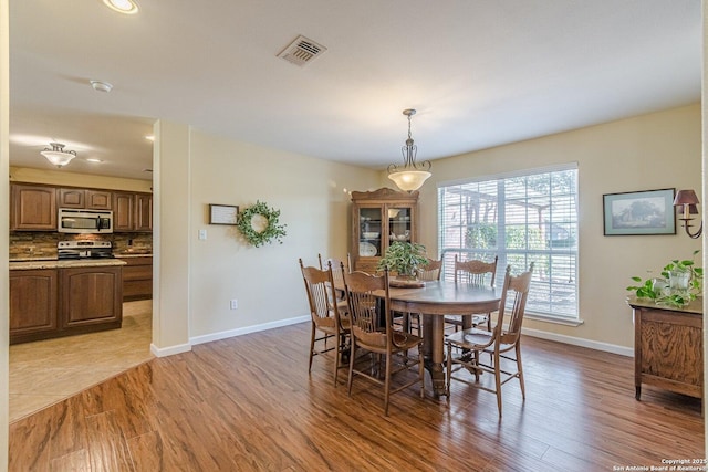 dining room with light wood finished floors, visible vents, and baseboards