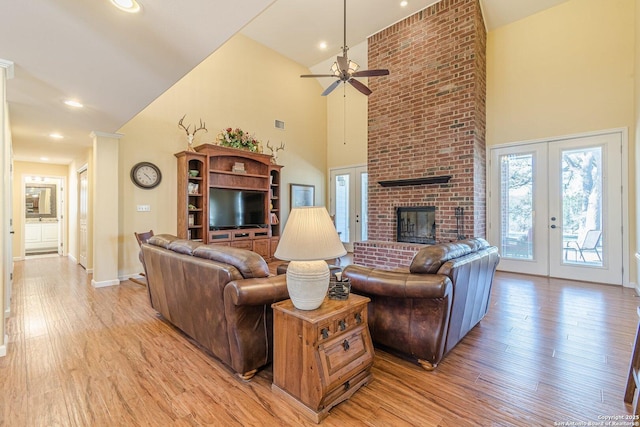 living area featuring a brick fireplace, light wood-style flooring, french doors, and a high ceiling