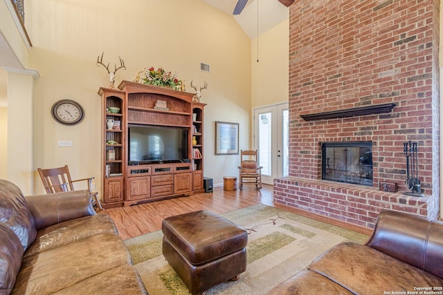 living room featuring visible vents, a fireplace, high vaulted ceiling, and light wood-type flooring