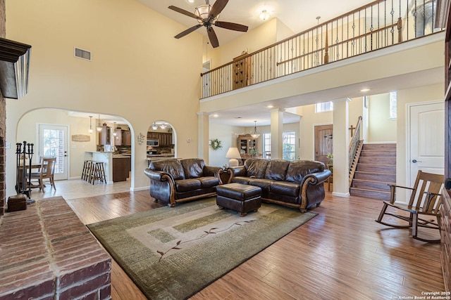 living area featuring arched walkways, plenty of natural light, ornate columns, and wood finished floors