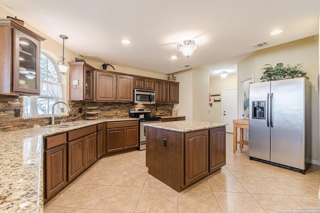 kitchen with a sink, a kitchen island, appliances with stainless steel finishes, light tile patterned floors, and decorative backsplash