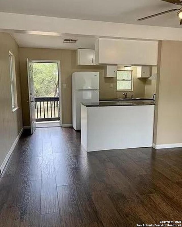 kitchen featuring a ceiling fan, dark wood-style floors, freestanding refrigerator, white cabinets, and dark countertops