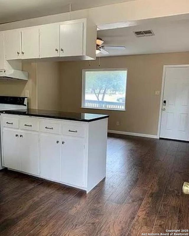 kitchen with dark countertops, visible vents, under cabinet range hood, stove, and dark wood-style flooring