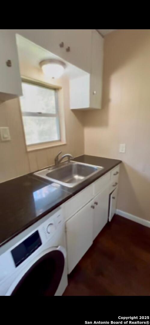 kitchen with a sink, washer / clothes dryer, dark countertops, white cabinets, and baseboards