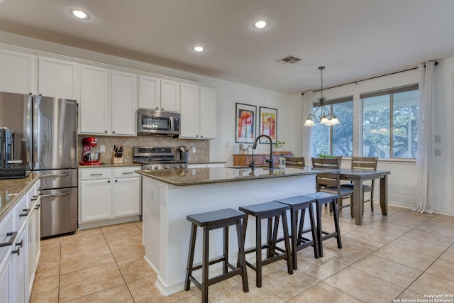 kitchen featuring visible vents, a sink, dark stone countertops, stainless steel appliances, and light tile patterned floors