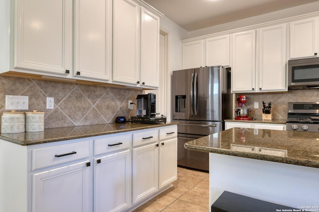 kitchen with light tile patterned floors, dark stone counters, decorative backsplash, appliances with stainless steel finishes, and white cabinetry