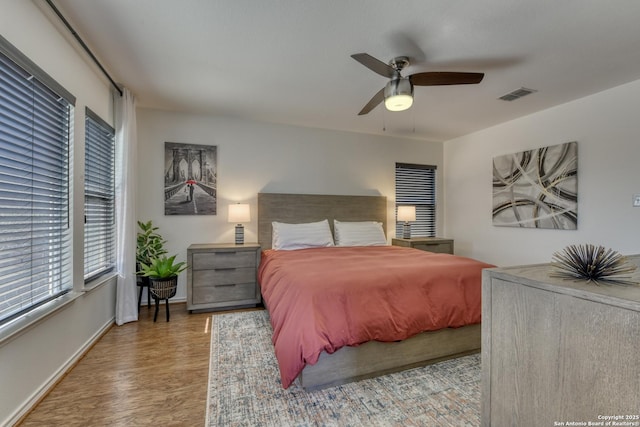 bedroom with ceiling fan, visible vents, baseboards, and wood finished floors