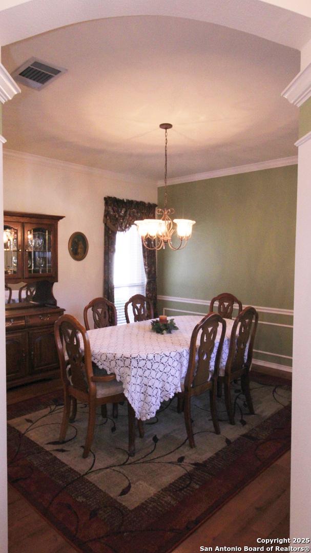 dining room featuring a notable chandelier, visible vents, wood finished floors, and ornamental molding