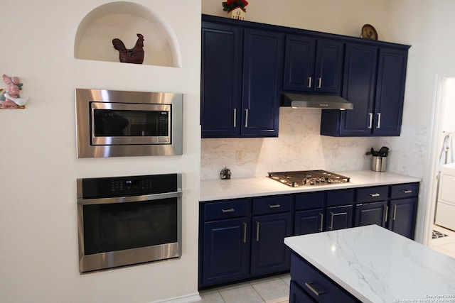 kitchen with blue cabinetry, stainless steel appliances, stacked washer and clothes dryer, under cabinet range hood, and backsplash