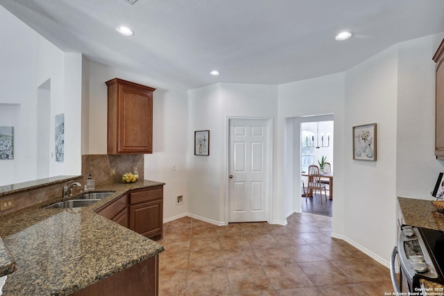 kitchen with a peninsula, dark stone counters, stainless steel electric range, a sink, and backsplash