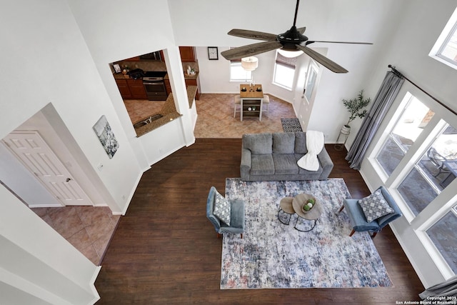 living room featuring baseboards, a ceiling fan, a towering ceiling, and wood finished floors