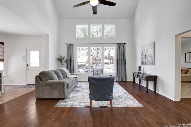 living area with a wealth of natural light, baseboards, wood finished floors, and a towering ceiling