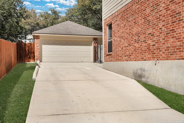 view of side of home featuring brick siding, fence, concrete driveway, a garage, and an outbuilding