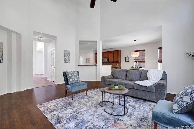 living area with baseboards, dark wood-type flooring, a high ceiling, and ceiling fan