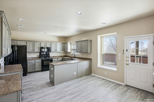 kitchen with a sink, black appliances, light wood-style floors, and gray cabinetry