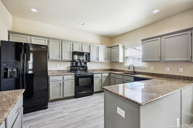 kitchen featuring light stone countertops, a peninsula, gray cabinets, a sink, and black appliances