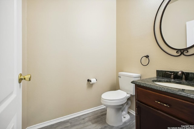 half bath featuring toilet, vanity, baseboards, and wood finished floors