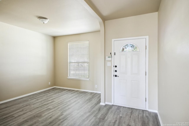 entryway featuring arched walkways, baseboards, and wood finished floors