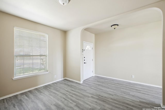 unfurnished room featuring arched walkways, baseboards, and wood finished floors