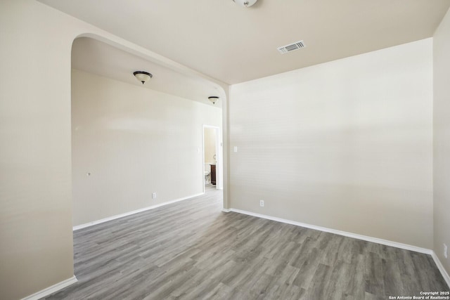 empty room featuring visible vents, baseboards, arched walkways, and wood finished floors