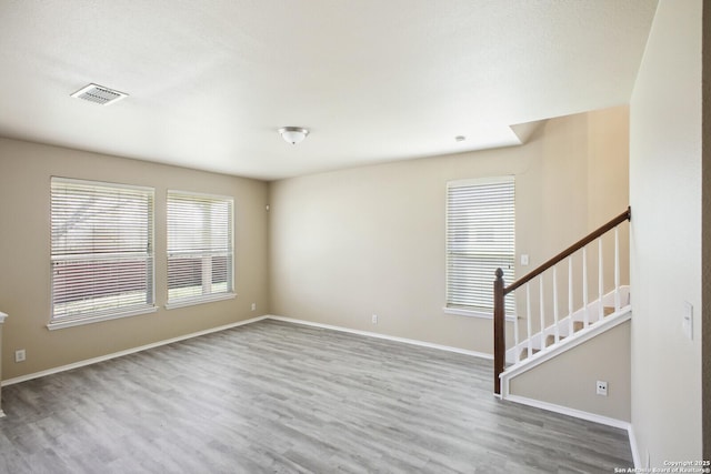 unfurnished room featuring visible vents, baseboards, wood finished floors, and stairway