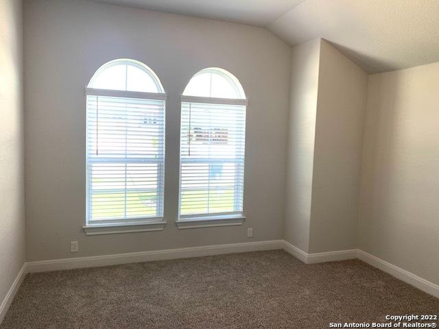 carpeted empty room featuring baseboards and vaulted ceiling